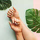 Beautiful manicured nails with white polish on hands over tropical leaves.
